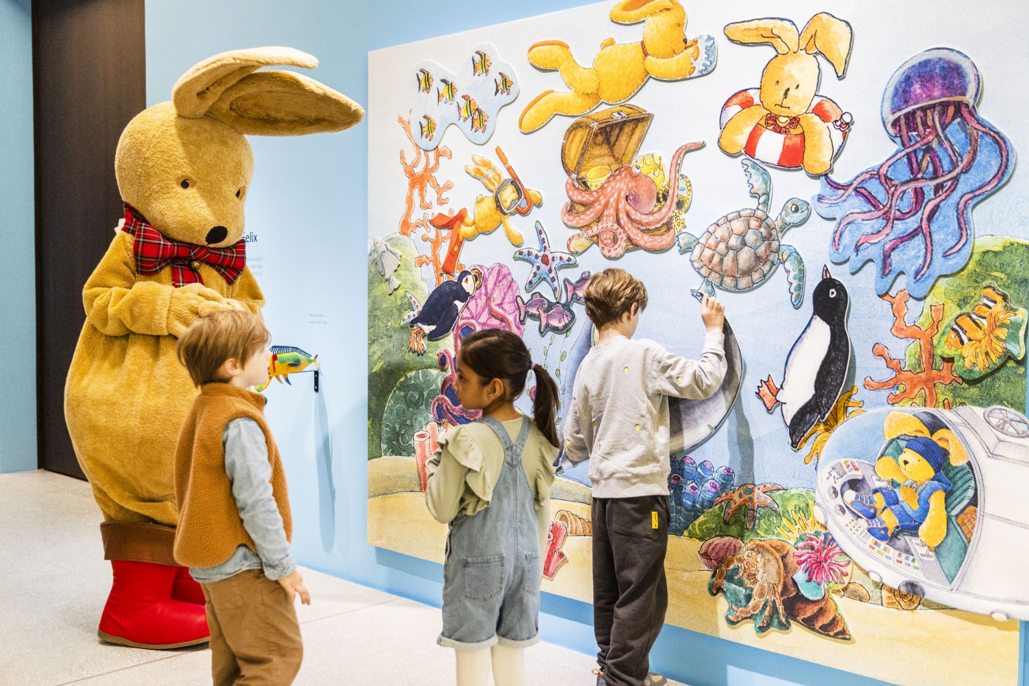 Der Hase Felix mit Kindern in der Ausstellung "Reiselustig". Foto: LWL / Hanna Neander © Felix, der Hase, Autorin: Annette Langen, Illustratorin: Constanza Droop ©