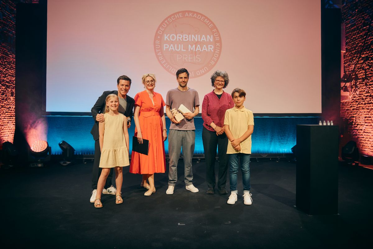 Korbinian-Preisträger Jona Manow (Mitte) mit Moderator Benedikt Weber, Akademiepräsidentin Dr. Claudia Maria Pecher, Anne Maar und den Leseluchs-Kindern Hannah Seuffert und Fabian Kaiser (v. l.) beim Paul Maar-Preis 2026 (Foto: Andreas Fuchs / Bayernwerk AG)